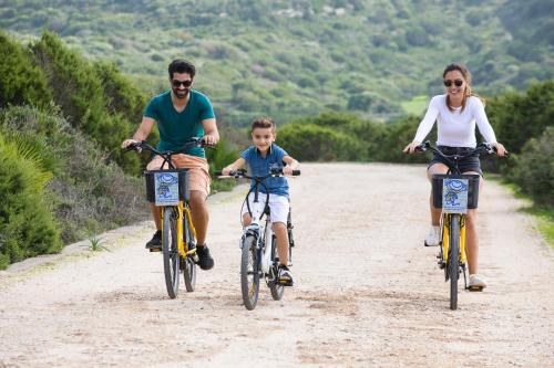 two adults and a child riding bikes on a dirt road at Lu' Hotel Maladroxia in SantʼAntìoco