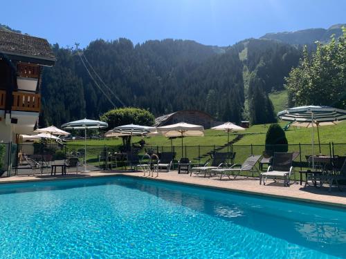 a swimming pool with tables and chairs and umbrellas at Hameau des Prodains - Hôtel in Morzine