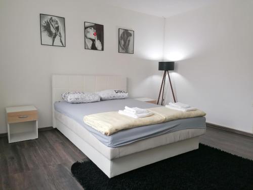 a bedroom with a white bed with a lamp and pictures on the wall at Apartment ELLA in Tuzla
