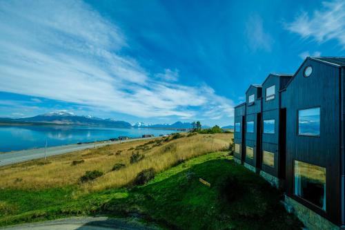 a black house on a hill next to a body of water at Weskar Lodge Hotel in Puerto Natales