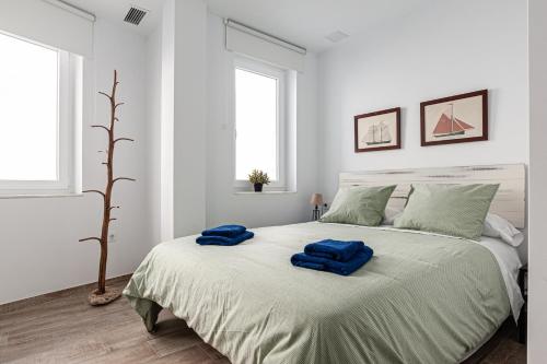 Un dormitorio blanco con una cama grande con toallas azules. en Apartamentos Wamba, en Conil de la Frontera