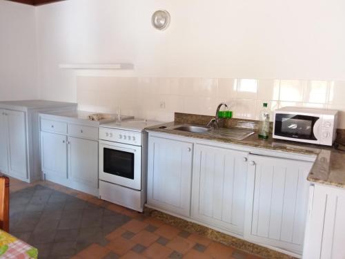 eine Küche mit weißen Schränken, einer Spüle und einer Mikrowelle in der Unterkunft Appartement ESCALE PARADIS in Aourir