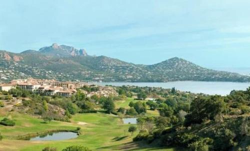 a view of a golf course with a lake and mountains at "Location Vue MER et ESTEREL", Cap Estérel Agay-Saint Raphaël, T2, piscines, parking, wifi in Saint-Raphaël