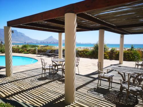 una terraza con mesas y sillas junto a una piscina en Cape Town Family Beachfront Apartment Leisure Bay en Ciudad del Cabo