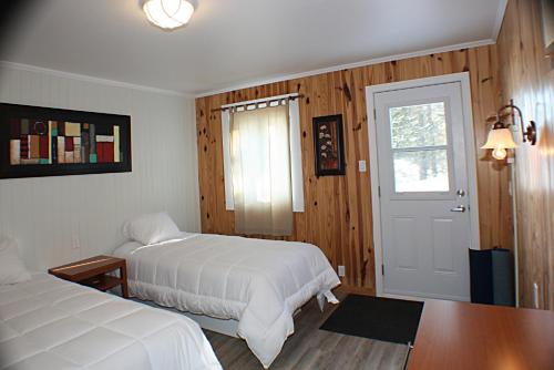 1 dormitorio con 2 camas, mesa y puerta en Auberge du sportif, en Saint-Tite-des-Caps