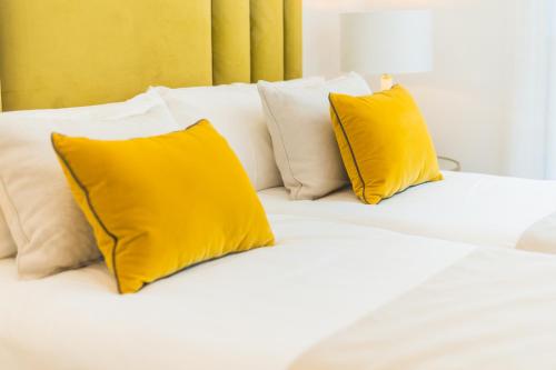 a white bed with two yellow pillows on it at Debambú Suites in Málaga