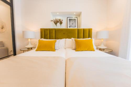 a bedroom with two white beds with yellow pillows at Debambú Suites in Málaga