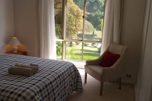 ein Schlafzimmer mit einem Bett, einem Stuhl und einem Fenster in der Unterkunft Sweet Holiday Home by the Golf Course in Canberra