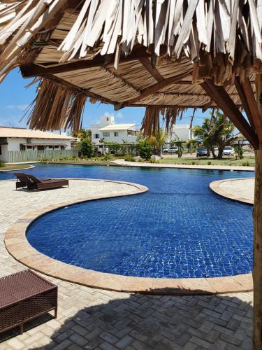 a swimming pool with a straw umbrella and a bench at Caly Pousada in São Miguel do Gostoso