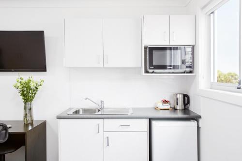 a white kitchen with a sink and a microwave at Aspire Newcastle in Newcastle