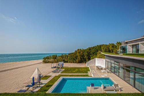 a house with a swimming pool next to a beach at Paradise Nurai Villa - 6 Bedrooms in Abu Dhabi