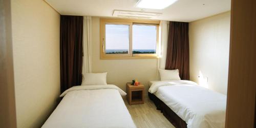 two beds in a room with a window at Hi Jeju Hotel in Jeju