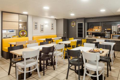 un restaurant avec des tables blanches et des chaises jaunes dans l'établissement B&B HOTEL Louveciennes, à Louveciennes