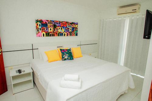 a bedroom with a white bed with a painting on the wall at Apartamento para família - Duplex Mont Moriá in Porto Seguro
