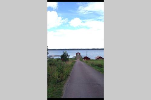 a road leading into a field with the ocean in the background at Idyllisk nybyggd stuga på Sollerön. in Sollerön