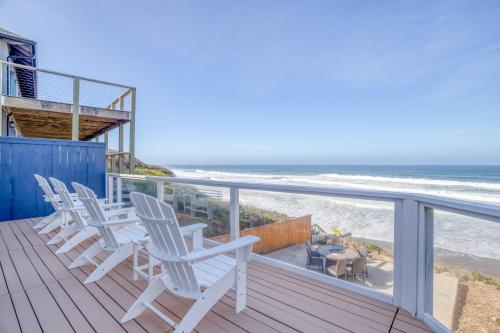 a row of white chairs on a deck with the beach at Beauty On The Beach in Depoe Bay
