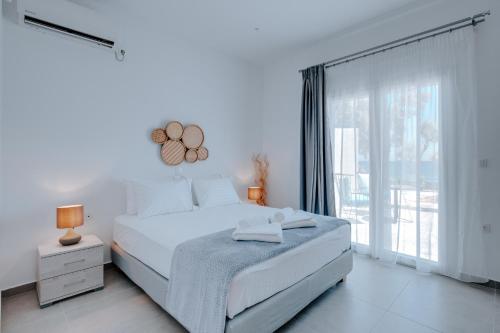 ein weißes Schlafzimmer mit einem Bett und einem großen Fenster in der Unterkunft Blue Magic Villas in Agia Paraskevi