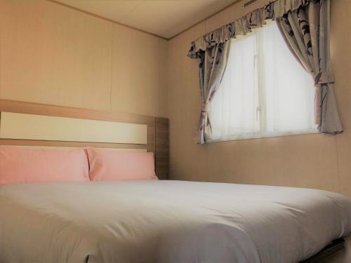 1 dormitorio con cama blanca y ventana en Birch Standard Holiday Home, en Chapel St. Leonards