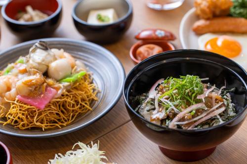 a table with two plates of food and a bowl of noodles at Dormy Inn Premium Nagasaki Ekimae in Nagasaki