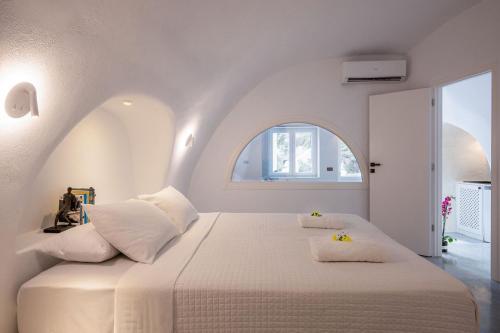 a white bedroom with a large bed with an arched window at Ecolodge Cave House in Vóthon