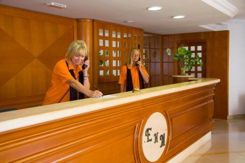 two women are talking on their cell phones behind a counter at Aparthotel Esquinzo Y Monte Del Mar in Playa Jandia