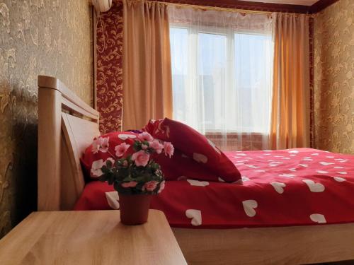 ein Bett mit roter Bettwäsche und eine Vase Blumen auf dem Tisch in der Unterkunft Уютная Однушка in Atyrau