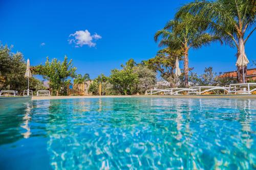 una piscina con agua azul y palmeras en Residence I Faraglioni en Scopello