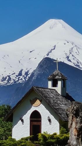 una iglesia con una montaña cubierta de nieve en el fondo en Hotel Salto del Carileufu en Pucón