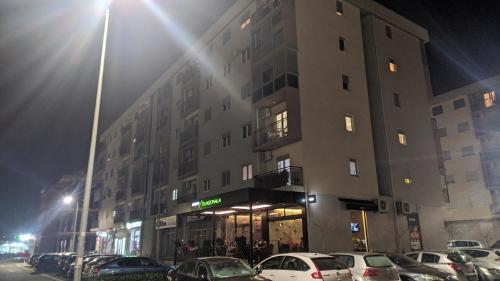 a tall building with cars parked in a parking lot at Guest House Mikeli (BESPL. DORUCAK)-(FREE BREAKFAST) in Podgorica