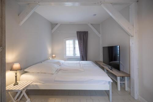 a white bedroom with a bed and a television at Altes Kontorhaus Backbord in Husum