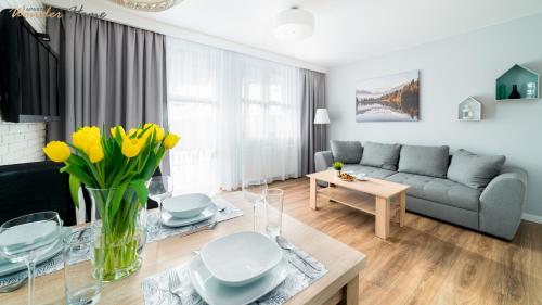 Una sala de estar con un sofá y una mesa con flores amarillas. en Wonder Home - Apartamenty Residence Karpacz blisko stoku narciarskiego, z balkonami i parkingiem, en Karpacz
