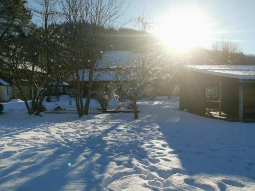 a snow covered yard with the sun shining behind a house at Gîtes Les Grandes Voies - Clé Vacances in Le Ménil