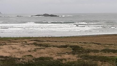 a beach with waves and an island in the ocean at Cabañas MAR BRAVA in Ancud