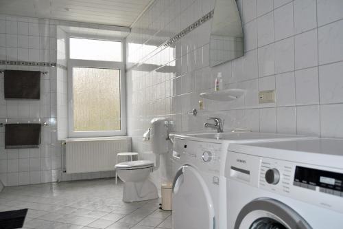 een witte badkamer met een wasmachine en een wastafel bij Alte Pastorei Minsen in Wangerland