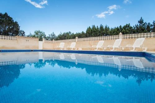 una piscina con sedie bianche e acqua blu di CASA GORKA Cala Saona a Cala Saona