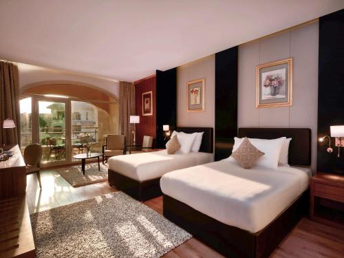 10月6日市にあるMövenpick Hotel Cairo - Media Cityのベッド2台とリビングルームが備わるホテルルームです。