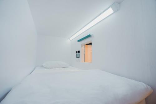 - une chambre avec un lit blanc et une petite fenêtre dans l'établissement Bobopod Paskal, Bandung, à Bandung