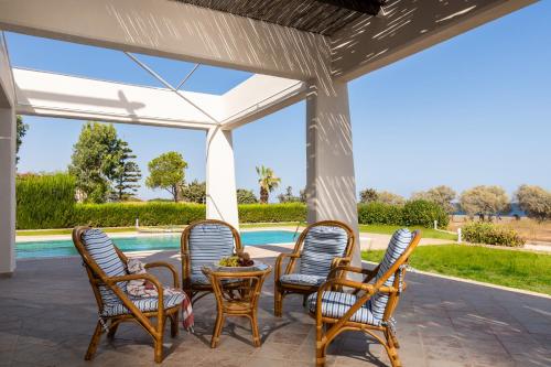 a patio with chairs and a table and a pool at The "Perfect Beach House" Villa in Lakhania