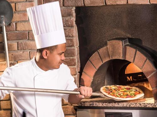 a chef putting a pizza into an oven at Novotel Abu Dhabi Gate in Abu Dhabi