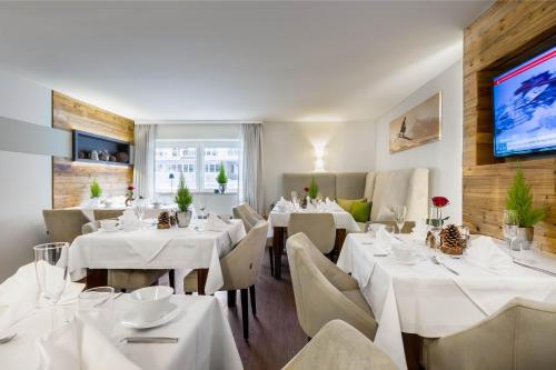 a restaurant with white tables and chairs and a tv at Boutique Hotel ANYBODY in Saalbach Hinterglemm