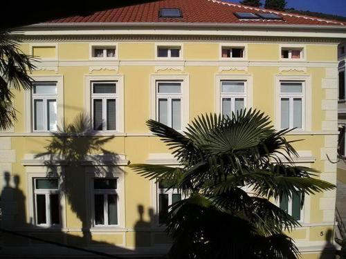 żółty budynek z palmą przed nim w obiekcie Apartment Damir w mieście Opatija
