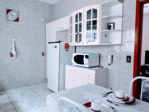 eine weiße Küche mit einem Tisch und einer Mikrowelle in der Unterkunft Casa confortável em Guaratinguetá in Guaratinguetá