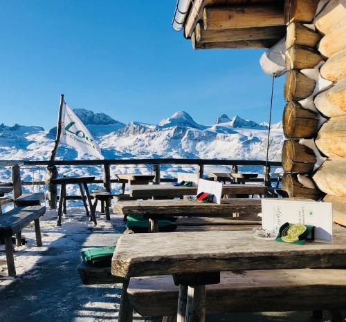 a row of wooden benches with snow covered mountains in the background at Lodge am Krippenstein in Obertraun