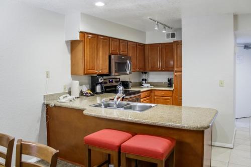 a kitchen with wooden cabinets and a sink and red stools at Hilton Vacation Club Polynesian Isles Kissimmee in Kissimmee