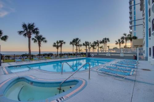 a swimming pool with chairs and the ocean in the background at Boardwalk Resort Oceanfront Condo by Hosteeva in Myrtle Beach