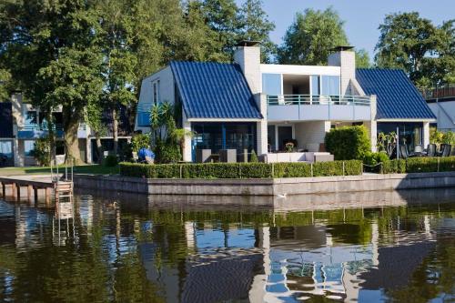 a house with a blue roof next to a body of water at Amsterdam / Loosdrecht Rien van den Broeke Village in Loosdrecht
