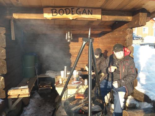 un hombre con una máscara sentado en una cabaña con una parrilla en Panoramaboende, en Torsby