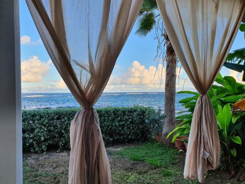 a view of the ocean from a room with a curtain at villa dans lo in Le Moule
