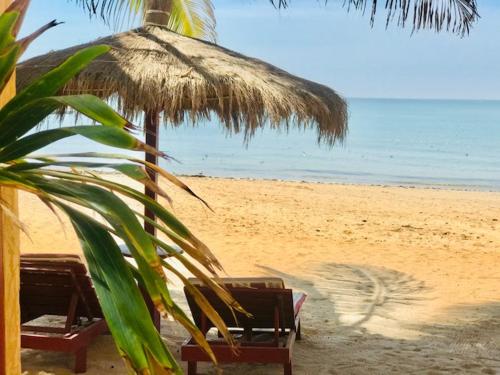 a beach with two chairs and a straw umbrella at Maison Couleur Passion in Nianing