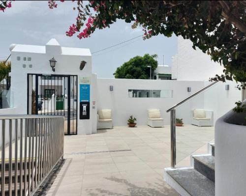 a white building with a gate and two white chairs at Apartamentos Acuario Sol in Puerto del Carmen